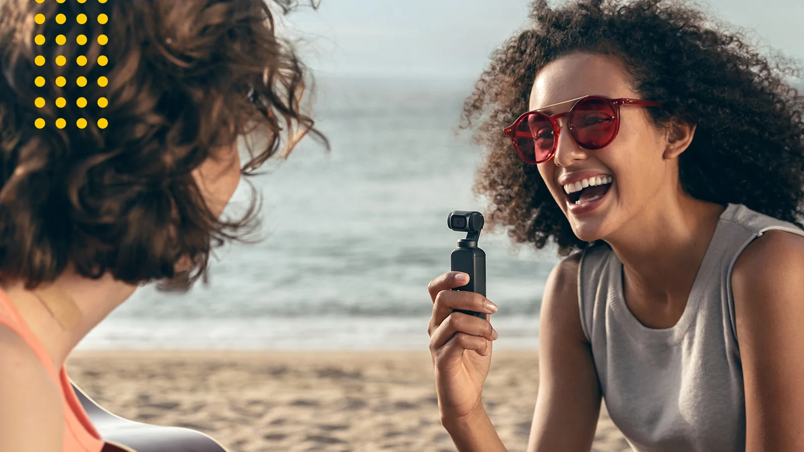 A woman uses the original DJI Osmo Pocket to film a guitarist on a beach in an official DJI photograph.